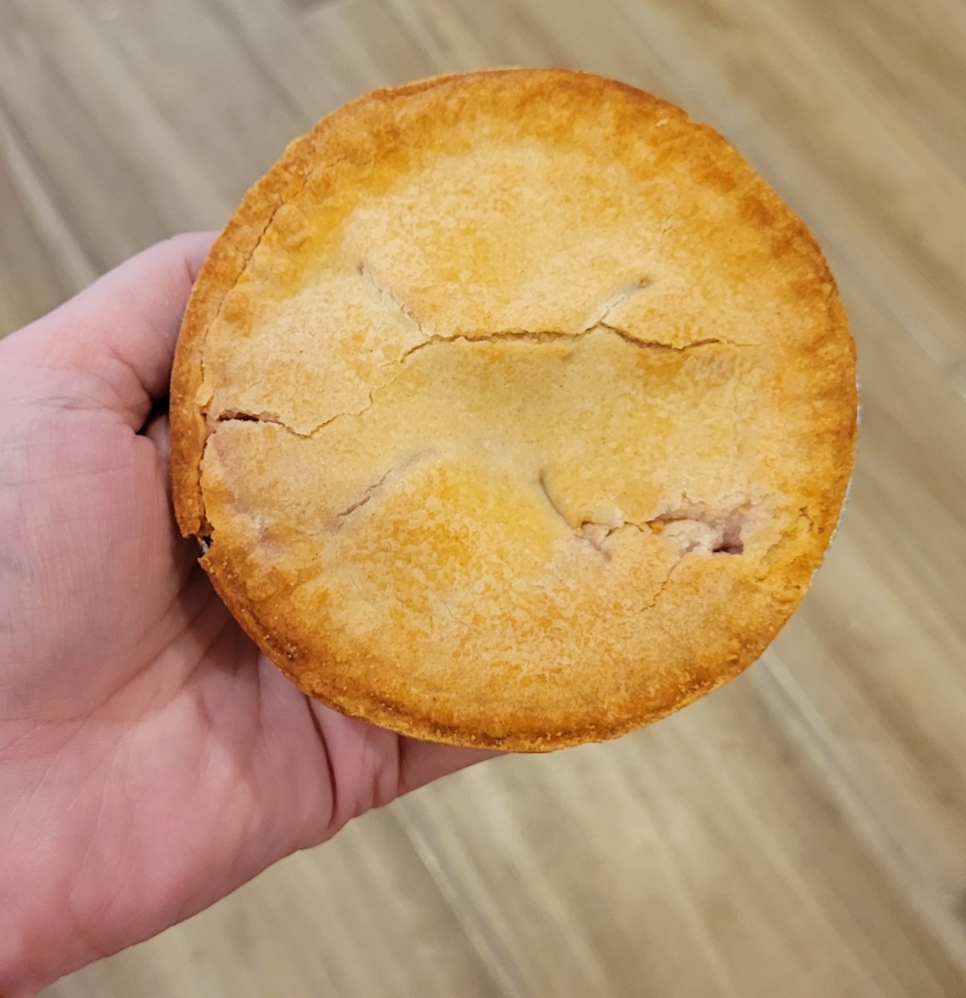 A white person's left hand is held palm-up from the left side of the image. Resting on and covering their fingers is a small cherry pie, about 3 inches across.