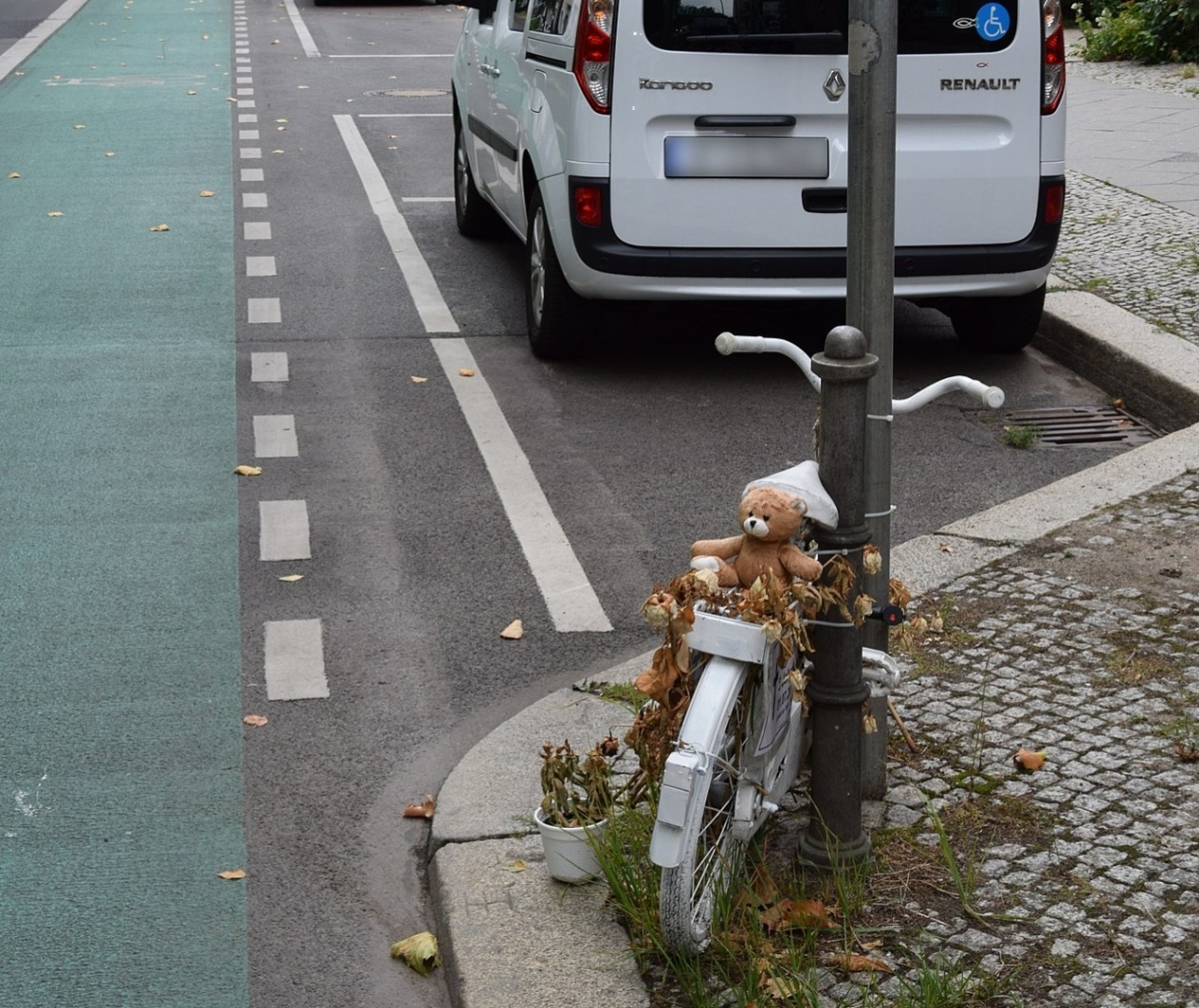 Ein Geisterrad lehnt angeschlossen an einer Laterne. Auf dem Rücksitz sitzt ein Teddybär.