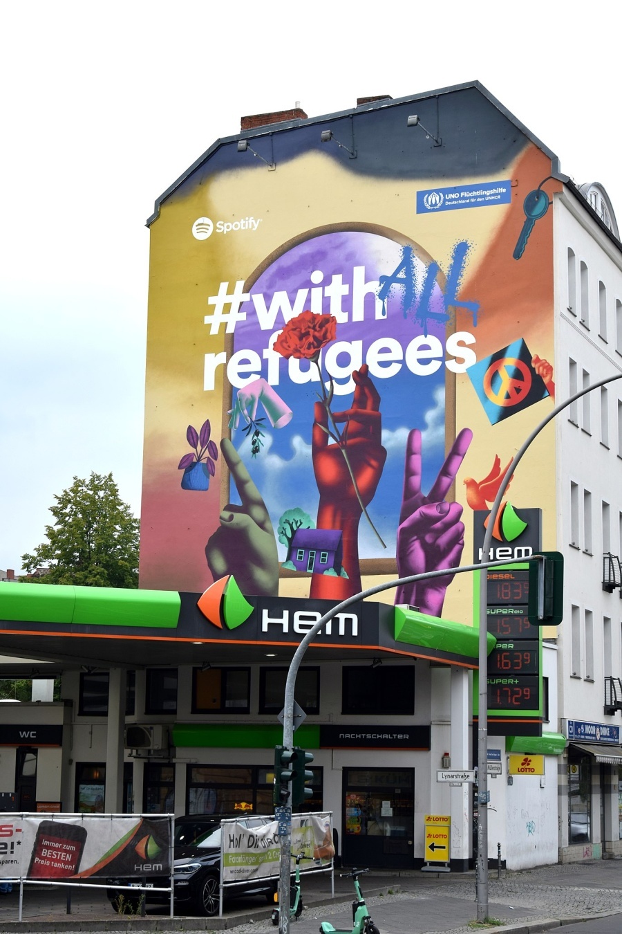 Mural an einer Hauswand in Berlin. Bild: verschiedenfarbige Hände sind nach oben gestreckt. Text: #with All refugees.